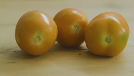 Zwei-Tomaten-Auf-Holztisch,-Eine-Weitere-Kommt-Hereingerollt