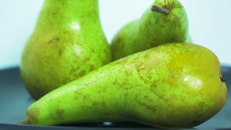 Fresh-big-green-pears-rotates-slowly-on-a-black-plate-on-light-blue-background,-healthy-food-concept,-extreme-close-up-shot,-camera-rotate-right