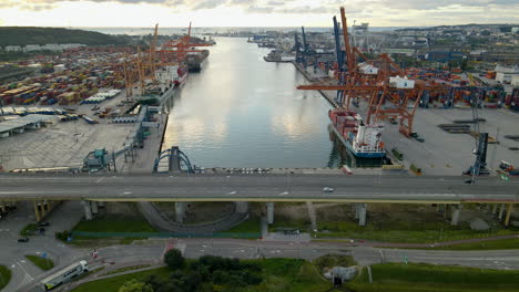 Schwenks-Aus-Der-Luft-Entlang-Der-Brücke-Und-Des-Hafens-Von-Gdynia-Mit-Riesigen-Kränen,-Die-Bei-Sonnenuntergang-Frachtcontainer-Auf-Frachter-Laden