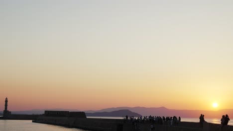 Schöner-Sonnenuntergang-über-Dem-ägäischen-Meer-In-Chania,-Touristen,-Die-Den-Alten-Venezianischen-Hafen-Mit-Historischem-Leuchtturm-Während-Des-Sommerabends-Genießen,-Besichtigungspunkt-In-Griechenland