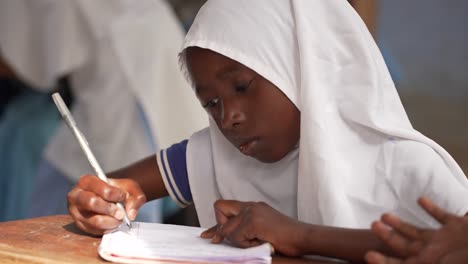 Islamisches-Mädchen,-Das-In-Der-Schule-Lernt,-Ein-Weißes-Kopftuch-Trägt-Und-In-Ihr-Notizbuch-Schreibt