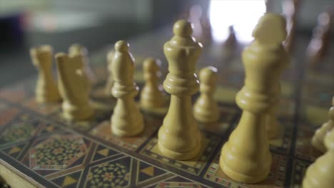Trucking-shot-from-left-to-right-of-old-white-chess-pieces-standing-on-a-chessboard-with-blur-background-at-home