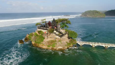Small-Hindu-temple-on-isle-with-bridge-to-Balekambang-Beach,-Indonesia,-arc-shot