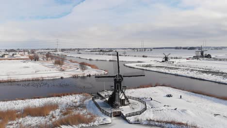 Dutch-snowy-windmill-and-frozen-canals,-aerial-view-over-countryside