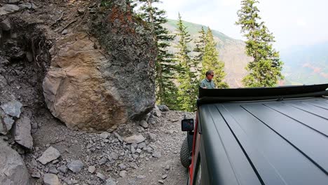 Man-directing-a-Jeep-around-a-hairpin-curve-in-Black-Bear-Trail-that-is-cut-into-the-side-of-a-mountain-in-the-San-Juan-Mountains-in-Colorado