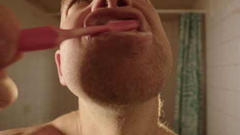 A-man-brushes-his-teeth-to-camera-in-a-bathroom