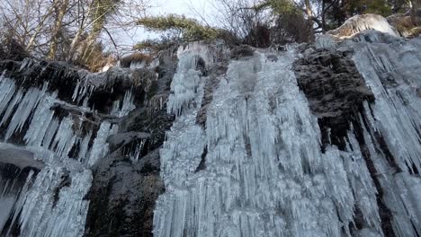 chunks-of-icicle-hanging-on-the-stone-wall-with-water-drops,-jungle-and-sky-on-the-top
