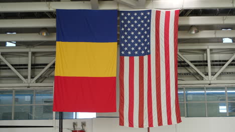 Bandera-De-Estados-Unidos-Y-Rumania-Colgando-Uno-Al-Lado-Del-Otro-En-El-Edificio-Del-Hangar