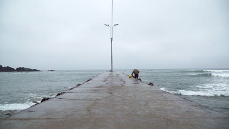 A-Fisherman-on-a-Pier-with-Ocean-Waves-in-San-Bartolo,-Lima,-Peru