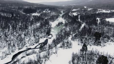 Wide-panoramic-aerial-tilt-from-snowy-forest-and-mountains-to-icy-lake