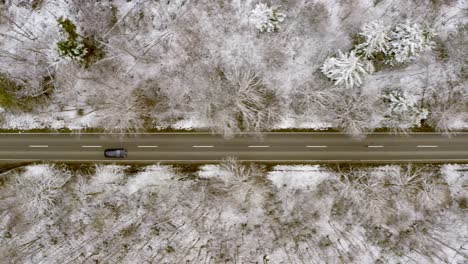 Flying-over-a-driving-car-by-drone,-tracking-it-when-it-drives-through-a-winter-forest-landscape