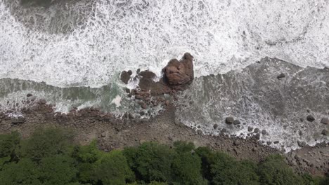 Birds-eye-view-aerial-shot-of-ocean-waves-crashing-into-rocks-on-the-shore
