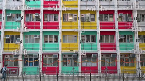 Menschen-Werden-Gesehen,-Wie-Sie-An-Einer-Farbenfrohen-Fassade-Eines-Sozialwohnungsgebäudes-In-Hongkong-Vorbeigehen