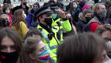 Two-Metropolitan-police-officers-wearing-protective-face-masks-stand-in-the-middle-of-a-protest-watching-and-monitoring-the-situation