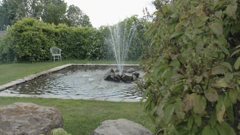 Reveal-of-a-beautiful-fountain-feature-on-a-gorgeously-landscaped-acreage-from-behind-a-hedge-on-a-cloudy-and-sunny-day