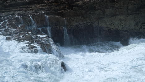 Wellenschlag-In-Felsen,-Schäumendes-Meerwasser-Fließt-Die-Felswand-Hinunter,-Turbulenter-Ozean