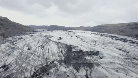Aerial-drone-view-above-the-blackened,-melting-Solheimajokull-Glacier,-in-cloudy-Iceland