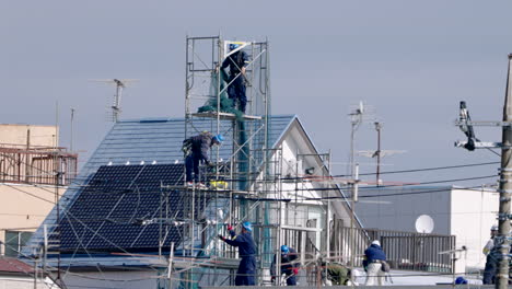 Japanische-Bauarbeiter-Arbeiten-Während-Einer-Pandemie-In-Tokio,-Japan,-Auf-Gerüsten-Auf-Dem-Dach-Mit-Sonnenkollektoren-Im-Hintergrund