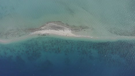 Rising-vertical-aerial-of-small-remote-sandy-islet,-coral-reef-lagoon