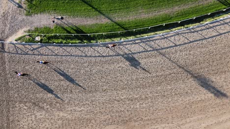 Vertical-straight-down-view-at-trainers-on-horseback-with-horses-galloping-on-the-racecourse-at-Hipodromo-Argentino-de-Palermo,-Buenos-Aires,-static-shot