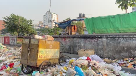 Trash-Cart-Beside-Rubbish-Next-To-Wall-With-Train-Going-Past-In-Dhaka,-Bangladesh