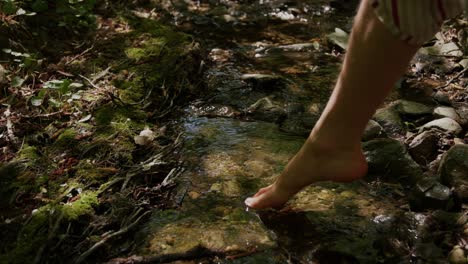 Man-carefully-stepping-barefoot-into-cold-natural-small-creek-close-up