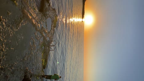 Vertikale-Aufnahme-Eines-Mannes,-Der-Bei-Sonnenaufgang-An-Der-Felsigen-Küste-Von-Enfeh-Im-Libanon-Fischt