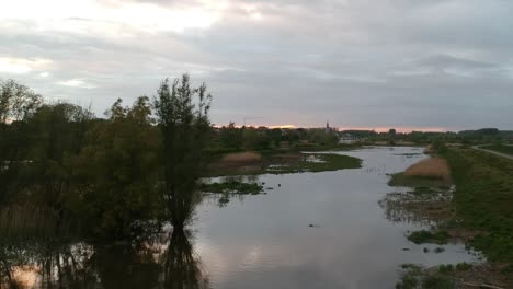 Rising-up-drone-flyover-rural-small-village-by-flooded-river-at-sunset