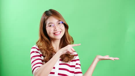 Young-woman-in-studio-pointing-to-object-to-be-graphically-entered-using-chroma-key