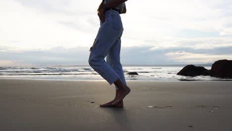 Young-beauty-female-walking-barefoot-on-sandy-coastline,-side-view