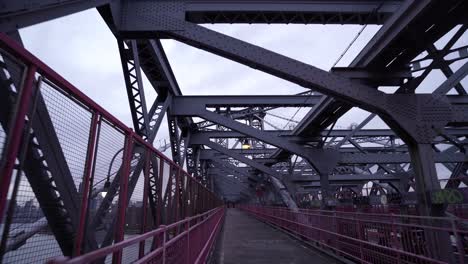 POV-walking-through-steel-structure-across-the-sidewalk-on-Brooklyn-Bridge,-New-York-City,-USA