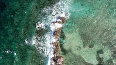Birdseye-Aerial-View-of-Tropical-Sea-Waves-Breaking-on-Small-Rocky-Islet,-Top-Down-Drone-Shot
