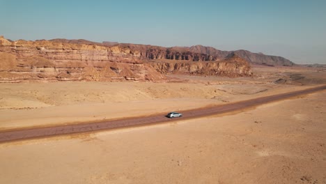 Eine-Folgende-Drohnenaufnahme-Eines-Autos,-Das-Auf-Einer-Straße-In-Einer-Großen-Wüste-Fährt,-Tolle-Aufnahme-Für-Übergänge-In-Wüstenszenen