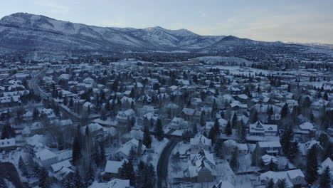 Beautiful-aerial-drone-shot-taking-houses-and-roads-covered-with-snow-over-Park-City,-Utah,USA-in-a-cold-wintry-evening
