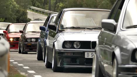 Procession-classic-collectors-club-BMW-E30-vehicles-travelling-along-forest-road-passing-close