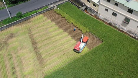 Aerial-drone-footage-Cultivated-rice-paddy-field,-farmer-harvesting-the-crops-with-multifunctional-paddy-harvesting-machine-rice-harvester-tractor-at-Doliu-Yunlin-City-Taiwan