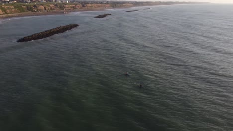 Aerial-orbiting-shot-of-a-person-with-kayak-rowing-in-wide-Atlantic-Ocean-front-to-cliffs-at-Acantilados-de-Mar-del-Plata-during-the-beautiful-sunset
