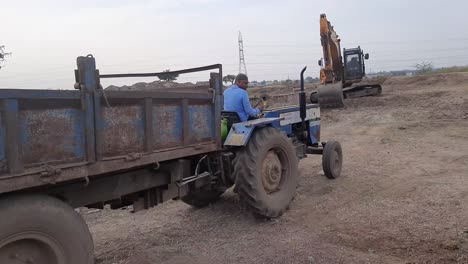 A-tractor-driver-drives-a-tractor-to-load-and-unload-soil-Moorum-by-excavator-machine-on-a-construction-site-in-India
