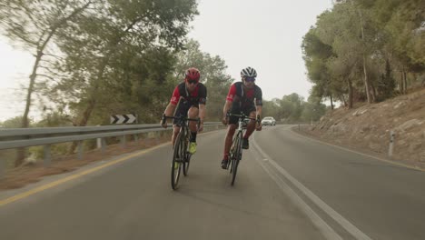 Cámara-Lenta-De-Dos-Profesionales-Ciclistas-De-Carretera-Montando-En-La-Carretera-Vacía-Del-Bosque