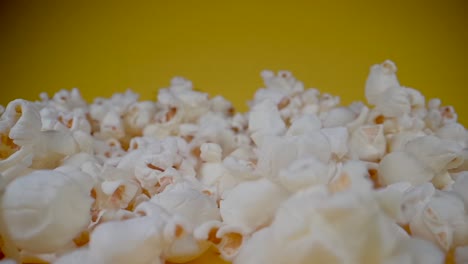 Close-up-dolly-shot-of-falling-sweet-popcorn-in-front-of-yellow-background-in-slow-motion