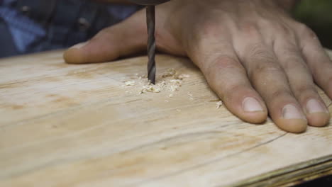 Crafstman-drilling-hole-in-wooden-plank-for-skateboard-wheels-to-attach,-close-motion-view