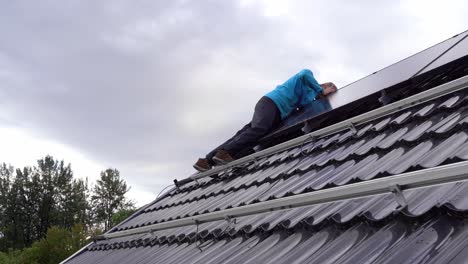 Worker-installing-solar-panels-on-roof-of-a-private-home-in-Norway---Working-on-top-of-roof-and-using-tools-to-secure-panels---Norway