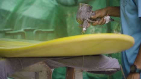 Slow-dolly-right-shot-of-shaper-painting-surfboard-with-paint-sprayer