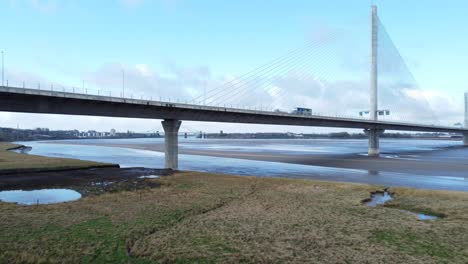 Mersey-gateway-landmark-toll-bridge-at-low-tide-with-river-marshland-aerial-view-slow-left-dolly