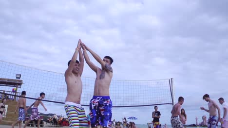 Two-Asian-males-congratulating-each-other-with-high-five-during-beach-side-volleyball-match-filmed-in-slow-motion