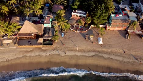 Aerial-fly-over-shot-of-Sayulita-main-beach-with-waves-crashing-on-the-beach-in-Mexico-during-sunset-hours