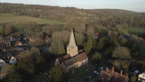 Golden-light-evening-aerial-over-St-James-Church-in-Shere,-Guildford