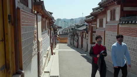 Zwei-Reisende-Mit-Atemschutzmasken-Reisen-Im-Dorf-Bukchon-Hanok-In-Seoul,-Südkorea