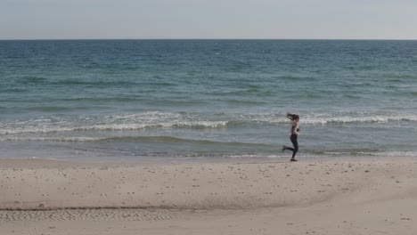 Junge-Fitness-Frau-Joggt-Am-Strand-Mit-Grünem,-Ozeanblauem-Himmel-Und-Hellem-Sand
