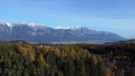 Flying-Over-Pine-Trees-In-Autumn-Foliage-With-View-Of-Rugged-Valley-In-Innsbruck,-Austria